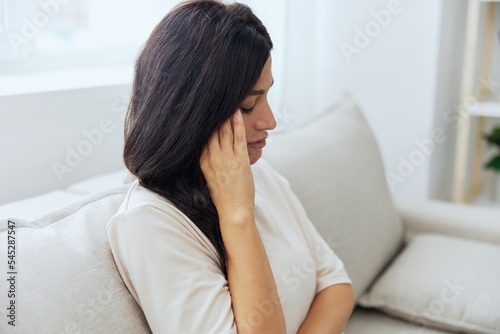 Headache woman sits at home on the couch and touches her head with her hands massage of the temples, high fever in case of illness, migraine