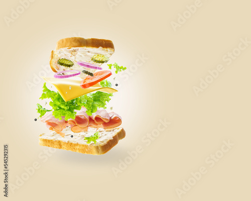 On a light beige background, a sandwich in a frozen flight. Pieces of meat, cheese and fresh vegetables on slices of bread. Minimalism. Vitamins, proteins, organic food.