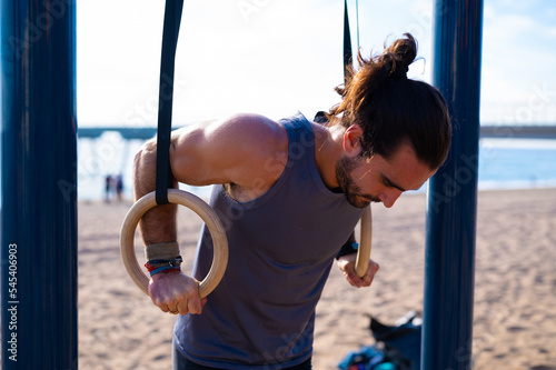 Adult man doing calisthenics exercises on rings outdoors. Sports concept.