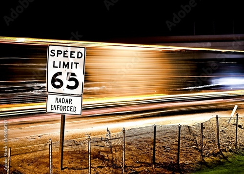 Pole with a speed limit 65 sign on the background of light trails of cars in a long exposure shot