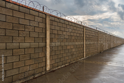 Brick wall that is lost from sight along, equipped in its upper part with concertinas, wires with cutting blades as an obstacle to cross it.