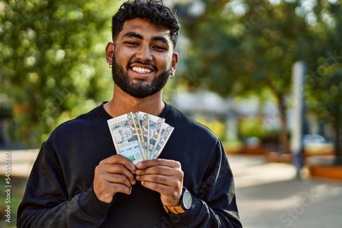 Young arab man smiling confident holding sol peruvian banknotes at park