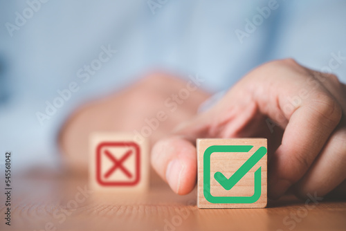 Businessman select green correct sign mark between Red Cross mark which print screen on wooden cube block for approve and reject business proposal concept.