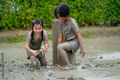 Asian girl and African American girl enjoy to look for frog and play in mud playground with fun and happiness together.