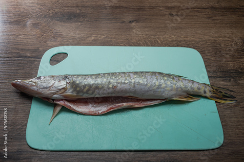  The cook cuts raw pike fish on a cutting board with a knife 