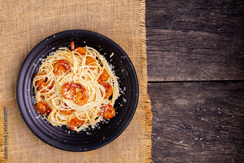 Delicious spaghetti pasta with prawns and cheese served in a black bowl on a black background table Italian recipe, tomato sauce, vegetables, and spices top view with copy space