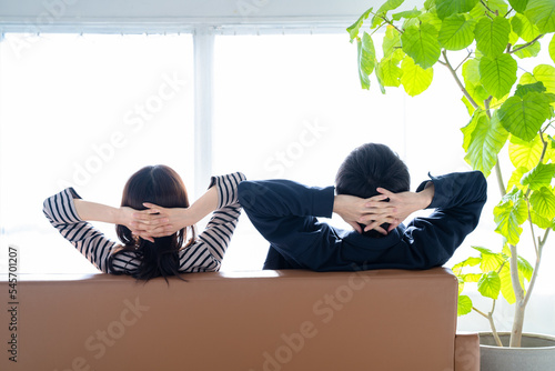 ソファに座り寄り添う後ろ姿の夫婦-明るい観葉植物のあるリビング