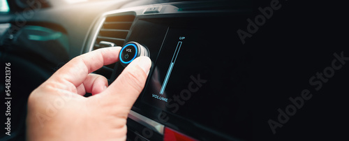 The driver hand is turning up or down the volume of the car music player or radio, panoramic banner with copy space on black background