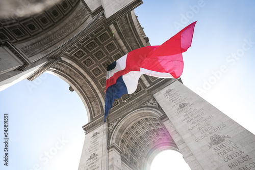 Wide angle photo with the National Flag of France waving under the Arch of Triumph landmark building during Armistice Day.