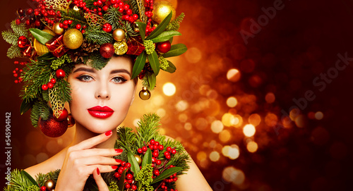 Christmas Woman Beauty. Beautiful Model in Fir Tree Wreath with Xmas Ornaments. Women Face Skin and Hands Winter Care. Fashion Girl with Red Lips Make up over Shining Lights Background