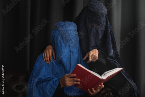 Afghan Muslim women with burka traditional costume, reading holy Quran against the dark background