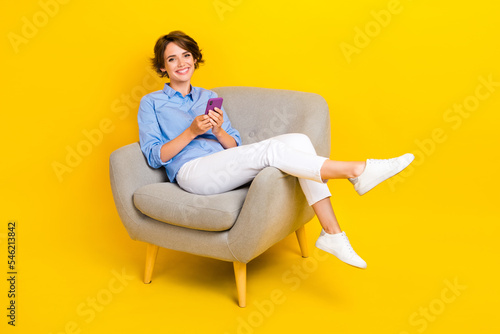 Full length photo of positive sweet girl dressed blue shirt chatting twitter facebook telegram modern gadget isolated yellow color background