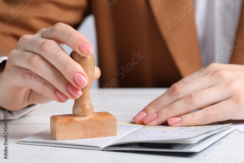 Ukraine, Lviv - September 6, 2022: Woman stamping visa page in passport at white wooden table, closeup