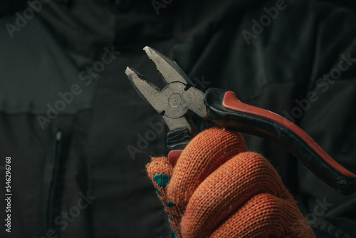 man's hand holding a black and red wire cutter plier open ready to cut form