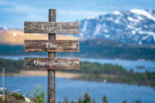 expect the unexpected quote written on wooden signpost outdoors in nature during blue hour. Mountain scenery background.