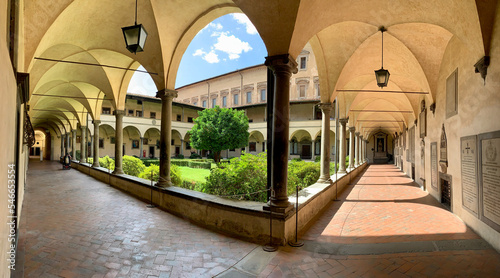 Cloister of San Lorenzo in Florence, Italy in wide-angle panorama with green courtyard leading to Laurentian library on sunny summer day
