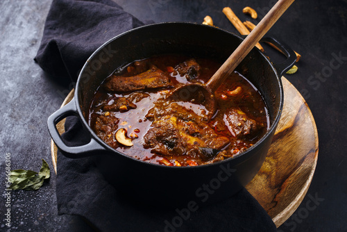 Traditional spicy Indian chicken Madras curry Rogan Josh with drumsticks, wings and roasted cashew nuts served as close-up in a saucepan