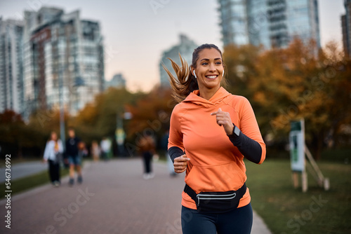 Happy sportswoman with earbuds running in park.