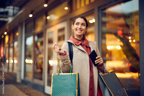 Young woman carrying shopping bags and feeling satisfied after spending day at mall.