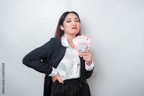 A portrait if a young businesswoman with a stack of money in Indonesian Rupiah in her hands isolated by white background