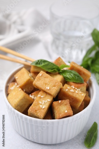 Bowl with delicious fried tofu, basil and sesame seeds on white table