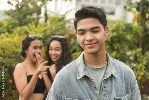 A man enjoys the attention he gets from two young women giggling in excitement behind him. Feeling handsome and confident, enjoying the attention. Outdoor scene,