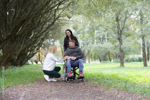 Smiling man in wheelchair and two women have fun in the park