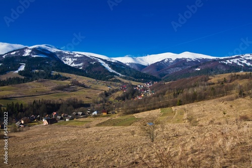 dreamy spring countryside sundawn, farming field at small village in Carpathian Mountains of Transcarpathia, dry grass and garden trees, Gemba peak lie in snow, protection and ecology background