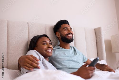 Loving Young Couple At Home Watching TV In Bed Together