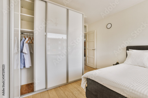 Home interior design of bedroom with bed and wooden wardrobe placed in corner near window in modern apartment