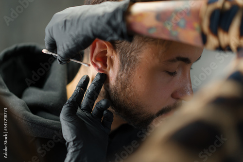 Tattoo piercing studio - a woman makes an ear piercing to a man to a guy