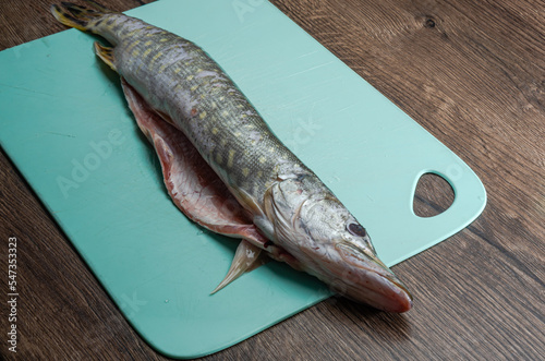 The cook cuts raw pike fish on a cutting board with a knife 