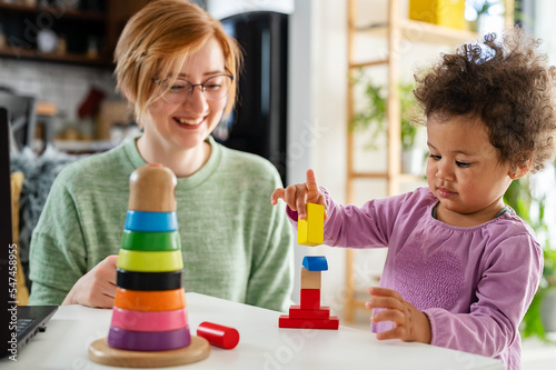 Mother looking at a child playing with an educational didactic toy. Young woman and child playing with didactic toys