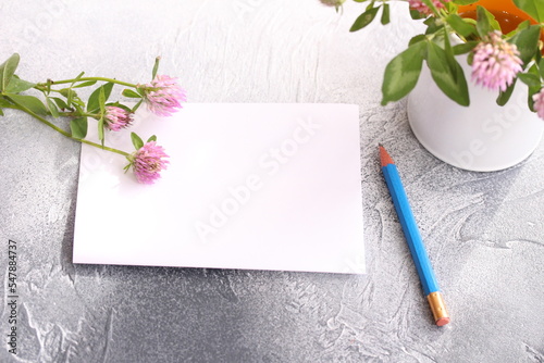 Empty note paper sheet with pencil. A sprigs of clover on the table and on the mug. Sweet moments in cozy home 