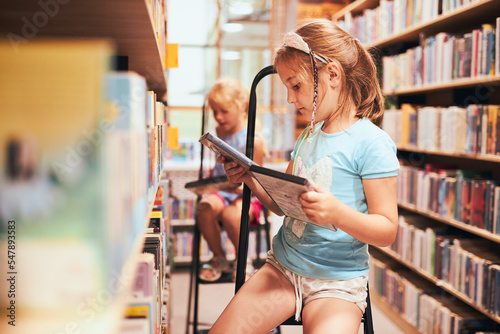 Schoolgirls looking for audio books in school library. Students choosing books. Elementary education. Doing homework. Back to school