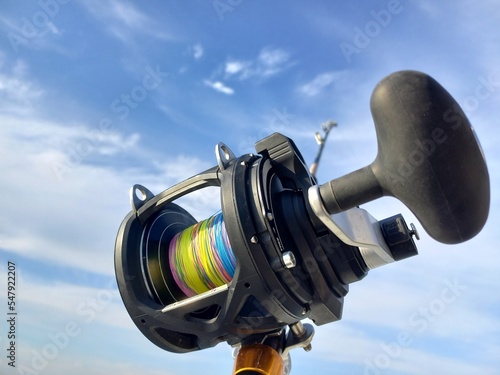 Mulinello di una canna da pesca con filo trecciato colorato e sullo sfondo un cielo azzurro