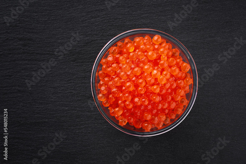 Artificial fake red caviar in glass bowl on dark background. Top view.