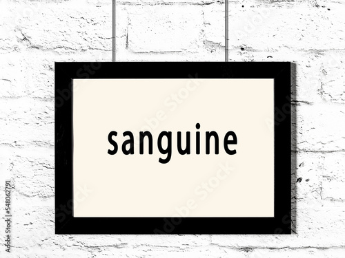 Black frame hanging on white brick wall with inscription sanguine