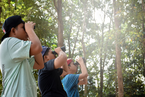 Portrait Asian boys using binoculars to watch birds in tropical forest with his friends, idea for learning creatures and wildlife animals outside the classroom, soft focus.