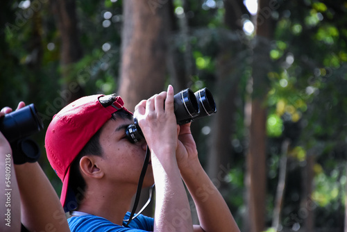 Portrait Asian boys using binoculars to watch birds in tropical forest with his friends, idea for learning creatures and wildlife animals outside the classroom, soft focus.