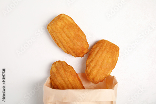 Paper bag with delicious madeleine cakes on white background, flat lay