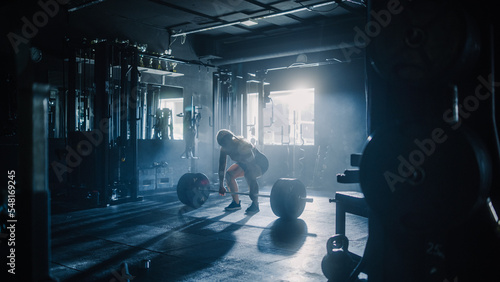 Professional Female Powerlifter in Position to Lift Heavy Weights in a Dark Gym. Portrait of an Athletic Woman Does a Barbell Lift. Extreme Workout, Exercise, Championship Training