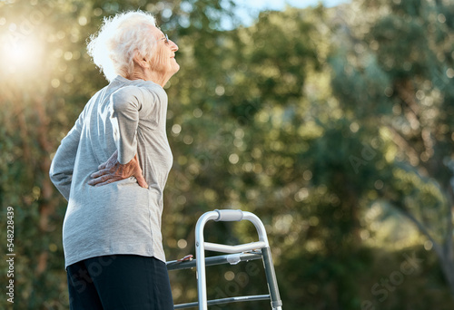 Senior woman, back pain and walking frame for rehabilitation at park for exercise for arthritis, fibromyalgia or osteoporosis problem. Old woman in nature for air, hope and freedom in retirement