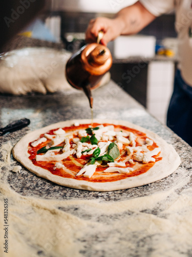 chef preparing pizza, oil can dripping oil on pizza