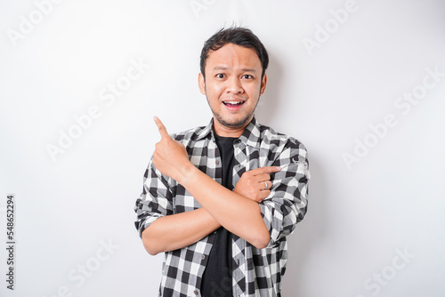Smiling Asian man wearing tartan shirt is pointing at the copy space on top of him, isolated by white background