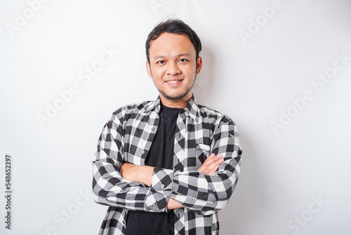 Portrait of a confident smiling Asian man wearing tartan shirt standing with arms folded and looking at the camera isolated over white background