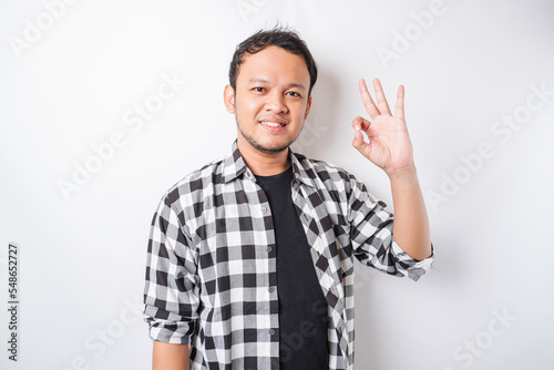 Excited Asian man wearing tartan shirt giving an OK hand gesture isolated by a white background