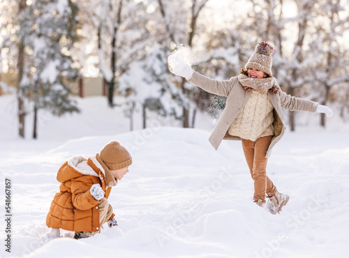 Two happy kids throwing snowballs at each other while playing with snow in winter park