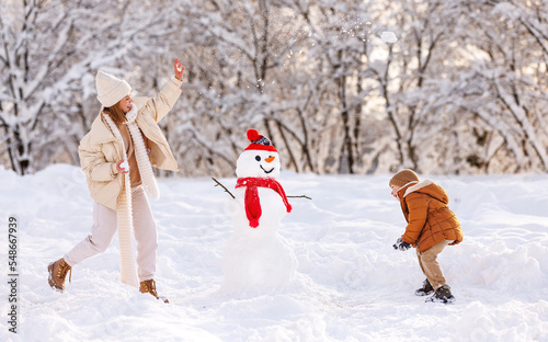 Happy overjoyed family mother and little son play snowballs outdoors in wintertime