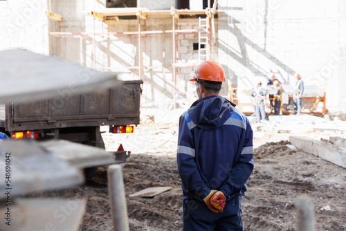 The foreman is standing at the construction site. The civil engineer observes the erection of the volume against the backdrop of the construction site.